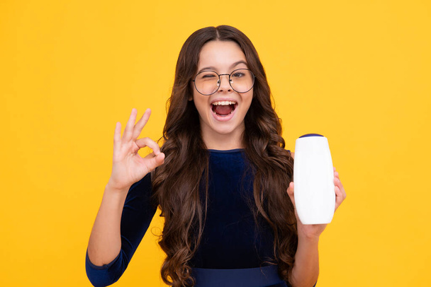 Child with shampoo conditioner. Daily cosmetic care. Teenager kid 12, 13, 14 years old hold bottle of hair and skin care. Beauty health and cosmetics. Happy face, positive and smiling - Φωτογραφία, εικόνα