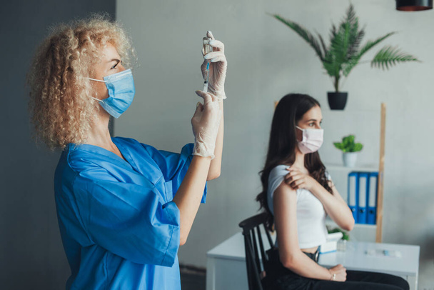 Kadın tıp doktoru şırınga iğnesiyle Covid-19 aşısını çıkarıyor. Hastanede eldiven takıp maske takıyordu. Pandemik önleme. Coronavirüs - Fotoğraf, Görsel