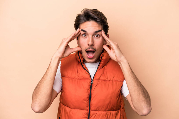 Young caucasian man isolated on beige background receiving a pleasant surprise, excited and raising hands. - Photo, Image
