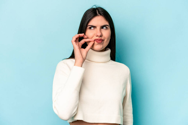 Young caucasian woman isolated on blue background with fingers on lips keeping a secret. - Foto, Bild