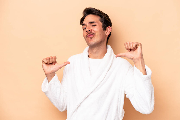 Young caucasian man wearing a bathrobe isolated on beige background feels proud and self confident, example to follow. - Photo, Image
