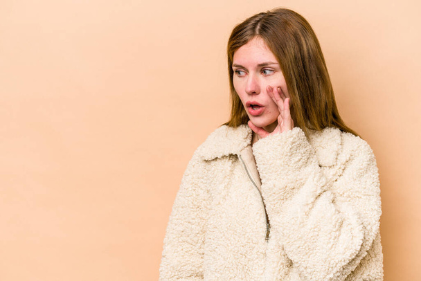 Young English woman isolated on beige background being shocked because of something she has seen. - Foto, Bild