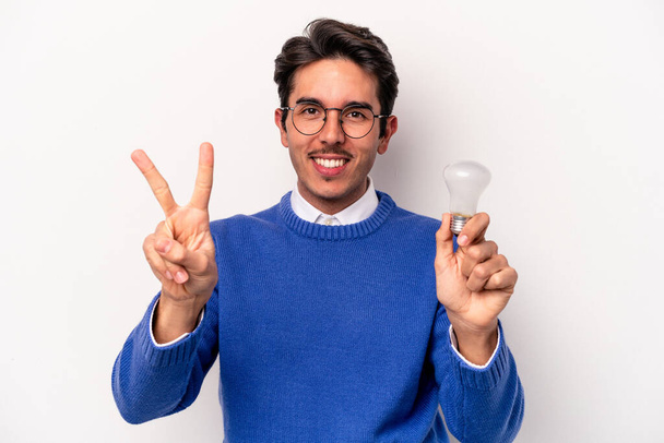 白い背景に孤立した電球を持っている若い白人男性は指で2番目を示しています. - 写真・画像