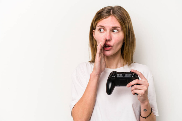 Giovane donna inglese che gioca con un controller di videogiochi isolato sfondo bianco sta dicendo una notizia segreta frenante caldo e guardando da parte - Foto, immagini
