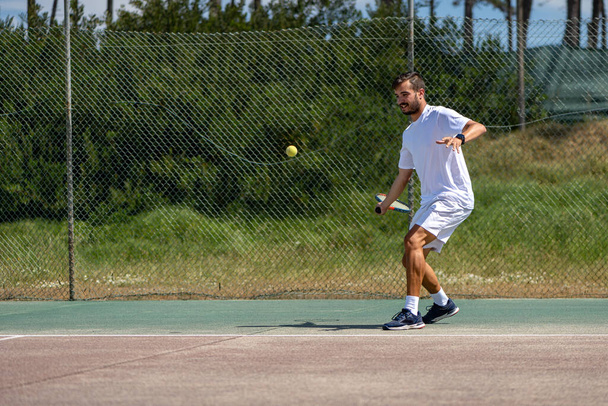 Tennis player hitting forehand at ball with racket on court. - Foto, Imagen
