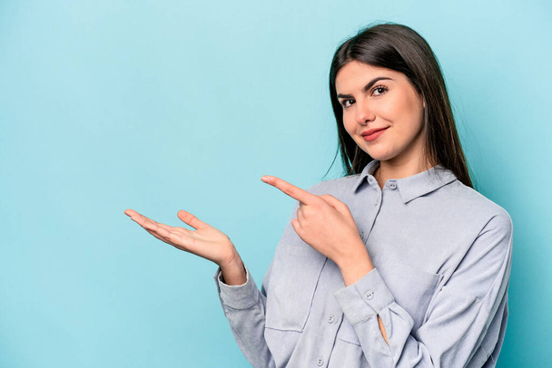 Young caucasian woman isolated on blue background excited holding a copy space on palm. - Photo, Image