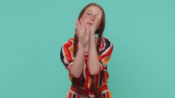 Funny joyful sincere redhead girl in dress making playful silly facial expressions and grimacing, fooling around showing tongue. Young beautiful ginger teenager child isolated alone on blue background - Footage, Video