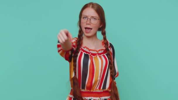 I choose you. Redhead girl pointing to camera and looking with playful happy expression, making choice, showing direction. Young one teenager ginger child kid indoor isolated on blue studio background - Footage, Video