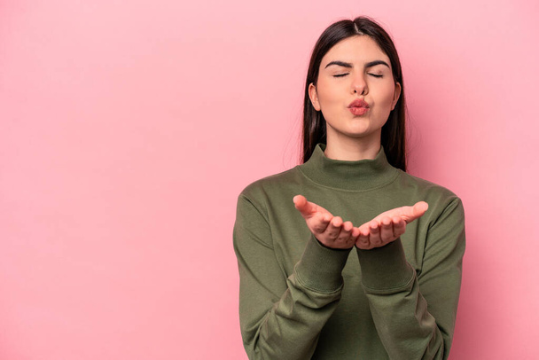 Young caucasian woman isolated on pink background folding lips and holding palms to send air kiss. - Foto, imagen