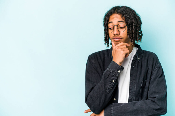 Junger afrikanisch-amerikanischer Mann isoliert auf blauem Hintergrund und schaut mit zweifelndem und skeptischem Gesichtsausdruck zur Seite. - Foto, Bild
