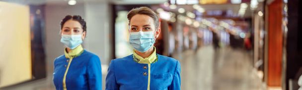 Kobiety stewardessy w maskach ochronnych i mundurach stewardessy podczas chodzenia po terminalu lotniska podczas pandemii - Zdjęcie, obraz