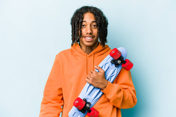 若いアフリカ系アメリカ人のスケーター男は青の背景に幸せ、笑顔と陽気に隔離された. - 写真・画像