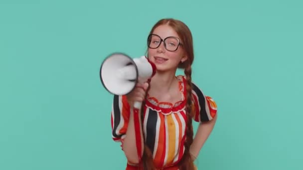 Smiling happy redhead girl talking with megaphone, proclaiming news, loudly announcing sale advertisement, warning using loudspeaker to shout speech. Young red hair teenager child on blue background - Footage, Video