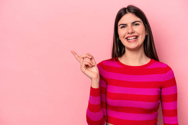 Young caucasian woman isolated on pink background smiling cheerfully pointing with forefinger away. - 写真・画像