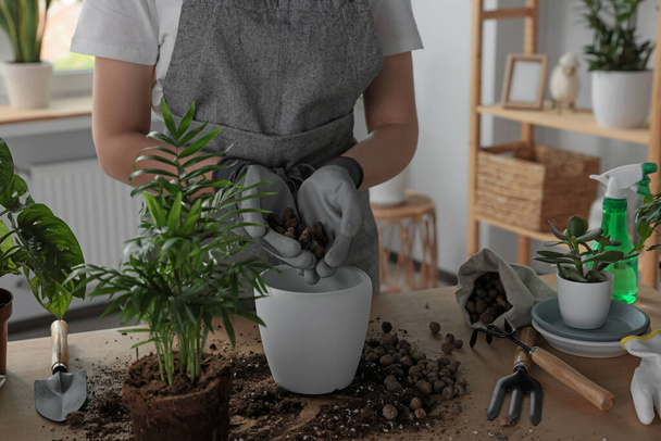Woman filling flowerpot with drainage at table indoors, closeup. Houseplant care - Foto, imagen