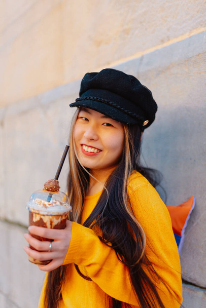 Азійська дівчина з радістю п "є шоколадний молочний коктейль на вулиці, спостерігаючи за містом в Європі.. - Фото, зображення