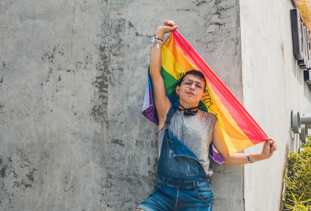 gay guy with glasses raising lgbt flag on gray city wall in sunny day isolated - 写真・画像