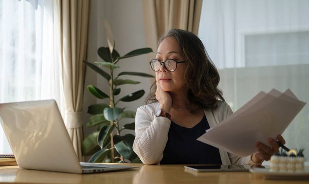 Pensativo anciano mujer madura viendo formación de negocios, webinar en línea en el ordenador portátil, mientras que el trabajo remoto desde casa. - Foto, Imagen