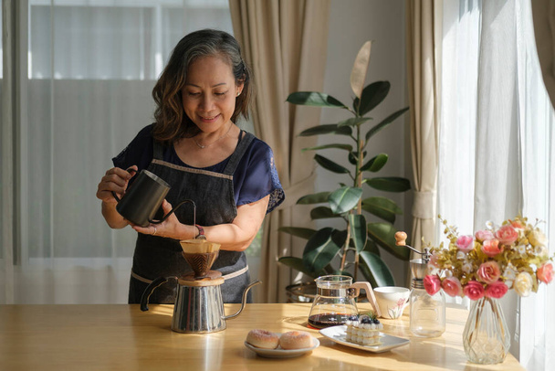 Feliz mujer de mediana edad preparando café para el desayuno en la cómoda cocina casera. Jubilación, estilo de vida saludable de las personas mayores. - Foto, Imagen