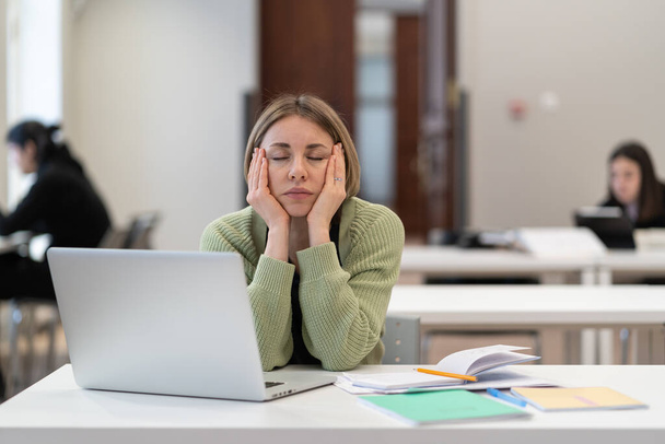 Yorgun, orta yaşlı bir kadın öğrenci. Masasında dizüstü bilgisayarla oturuyor. İnternette uyukluyor. Yorgunluk çalış - Fotoğraf, Görsel