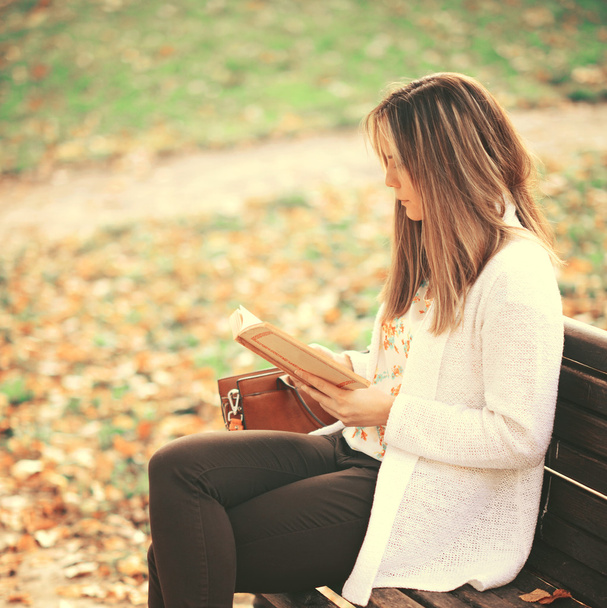 Kobieta czytająca książkę na ławce w parku jesień - Zdjęcie, obraz