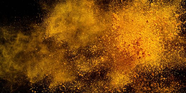 Explosion, Splashes of turmeric on a black background. India Seasoning. The orange powder of the turmeric root. Explosion of powder - Photo, Image