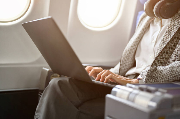 Wspaniała bizneswoman w samolocie w fotelu klasy biznes, używająca laptopa do pracy nad swoim biznesowym projektem. Miejski styl życia z koncepcją transportu. przycięty obraz - Zdjęcie, obraz