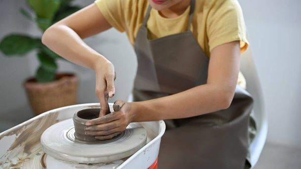 przycięty obraz, kobiece dłonie robiące ceramiczne kubki na kole garncarskim w warsztacie rękodzieła. - Zdjęcie, obraz