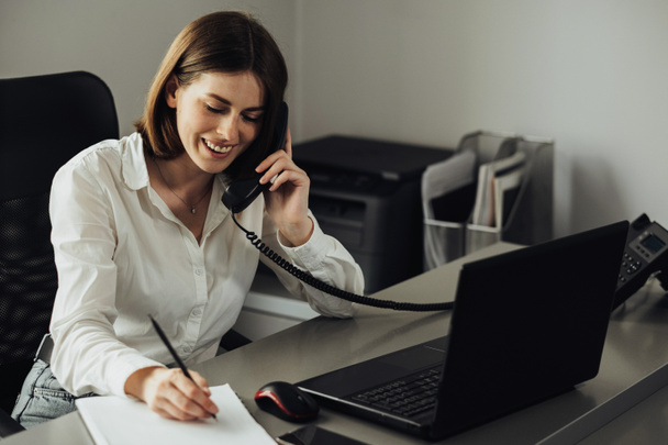Жінка-бухгалтер, що працює в офісі, повідомлення жіночої нотатки під час здійснення дзвінка на бізнес-телефон
 - Фото, зображення