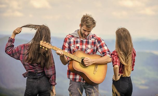Nothing but friends and guitar. People relaxing on mountain top while handsome man playing guitar. Hiking entertainment. Peaceful place. Melody of nature. Hiking tradition. Friends hiking with music. - Photo, image