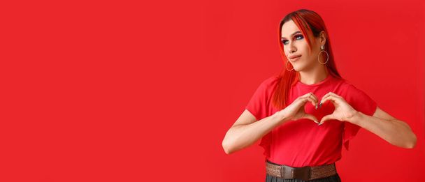 Stylish transgender woman making heart with hands on red background with space for text - Фото, изображение