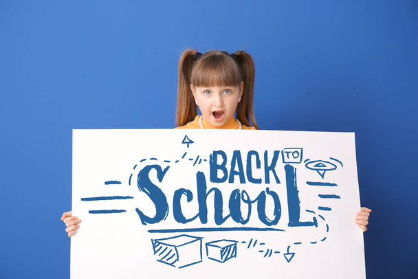 Сюрприз маленькая девочка держит плакат с текстом назад в школу на синем фоне - Фото, изображение