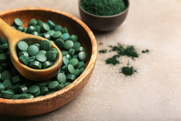 Bowl of spirulina pills with spoon on beige background, closeup - Photo, Image