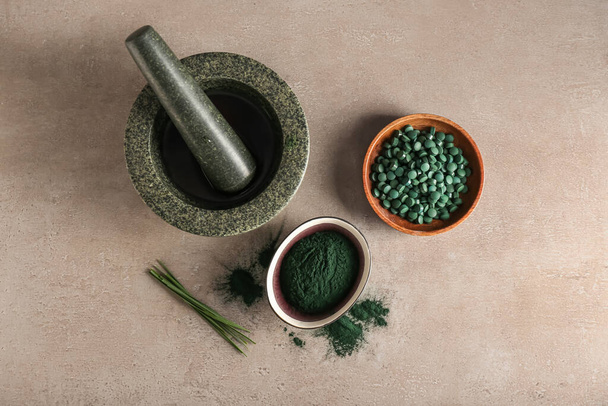 Bowls of spirulina powder, pills, mortar and pestle on beige background - Photo, Image
