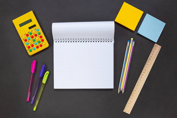 Блокнот, желтый калькулятор, ручки и карандаши, наклейки, линейка на черном фоне. Канцелярские принадлежности для бизнеса, учебы. Концепция возврата к школе, финансам. Копирование пространства - Фото, изображение