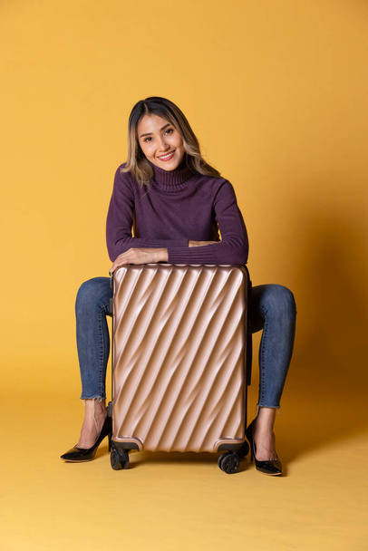 красивая брюнетка женщина в соломенной одежде и сумка на бежевом фоне со старым чемоданом, глядя в сторону, - Фото, изображение