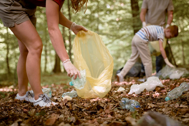 Крупним планом жіноча рука збирає пластикову пляшку з лісу
  - Фото, зображення