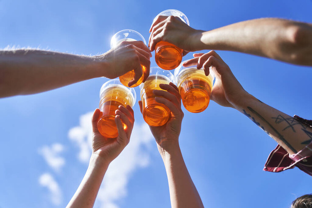 Low angle view of hands toasting beer on blue sky at festival  - Foto, afbeelding