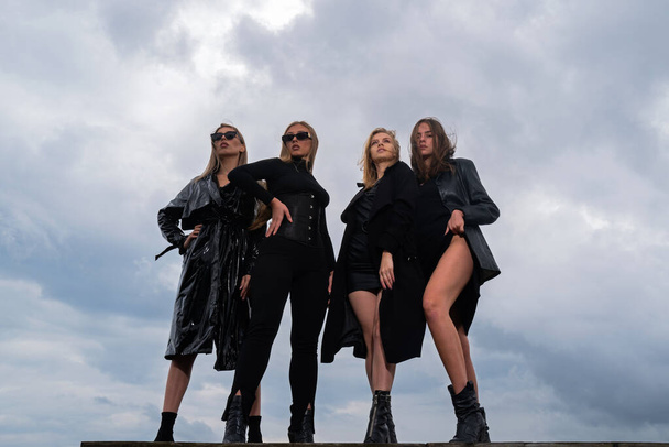 Fashion portrait of group fashion models girls posing outdoor, black style outfit against sky. Attractive young vogue women - Foto, immagini