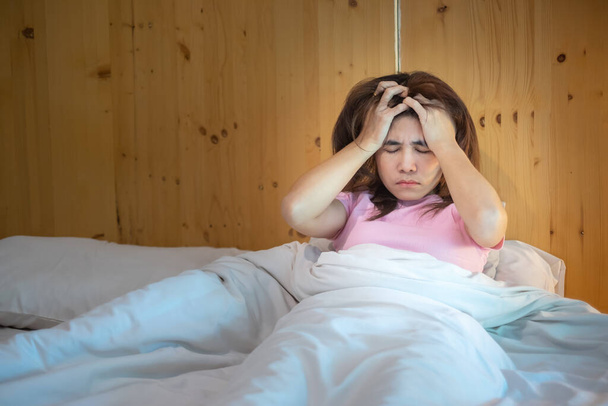 egy nőnek migrénes fejfájása van, miközben otthon fekszik az ágyban. álmatlanság, álmatlanság, fáradtság, szenvedés és stresszes fogalmak - Fotó, kép