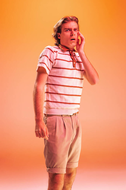 Portrait of young emotive man posing with shocked facial expression isolated over orange background in neon light. Expressive news. Concept of youth, fashion, lifestyle, emotions. Copy space for ad - Foto, Bild