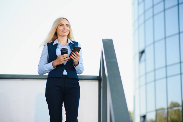 Beautiful Woman Going To Work With Coffee Walking Near Office Building. Portrait Of Successful Business Woman Holding Cup Of Hot Drink - Foto, Bild