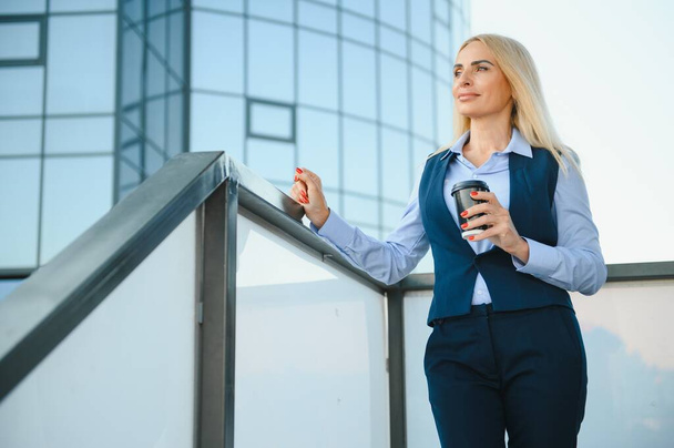 Beautiful Woman Going To Work With Coffee Walking Near Office Building. Portrait Of Successful Business Woman Holding Cup Of Hot Drink - Zdjęcie, obraz