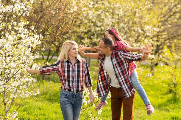 Happy parents mom and dad, daughter, young family outdoors in spring against the background of blooming apple and cherry trees. - Fotografie, Obrázek