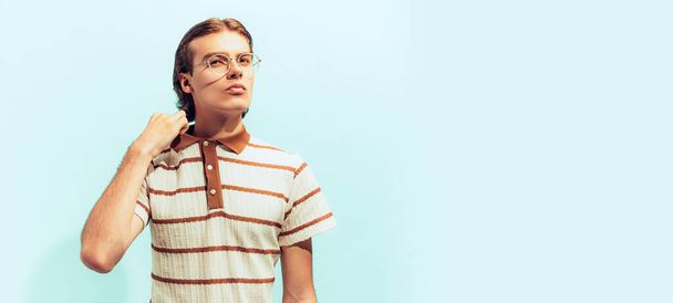 Potrait van jonge man in casual T-shirt poseren geïsoleerd over lichtblauwe studio achtergrond. Ziet er serieus en geconcentreerd uit. Concept van jeugd, mode, levensstijl, emoties. Kopieer ruimte voor advertentie - Foto, afbeelding
