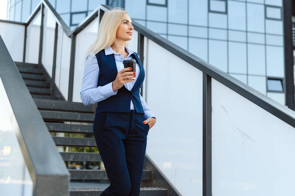 Beautiful Woman Going To Work With Coffee Walking Near Office Building. Portrait Of Successful Business Woman Holding Cup Of Hot Drink - Foto, Imagen