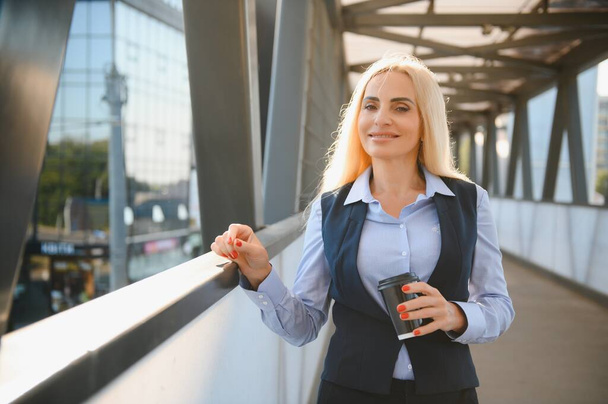 Beautiful Woman Going To Work With Coffee Walking Near Office Building. Portrait Of Successful Business Woman Holding Cup Of Hot Drink - Фото, зображення