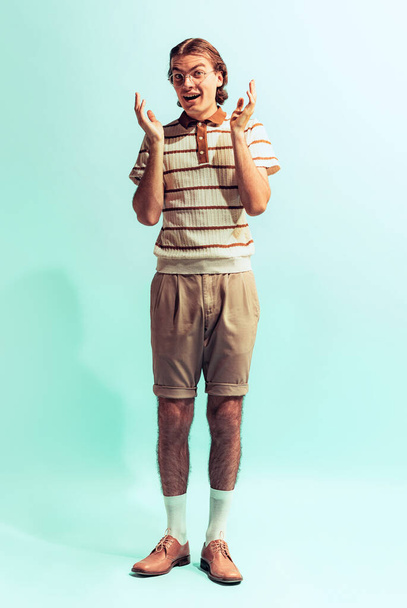 Full-length portrait of young man in retro style outfit posing isolated over light blue studio background. Looks excited. Concept of youth, fashion, lifestyle, emotions. Copy space for ad - Фото, зображення