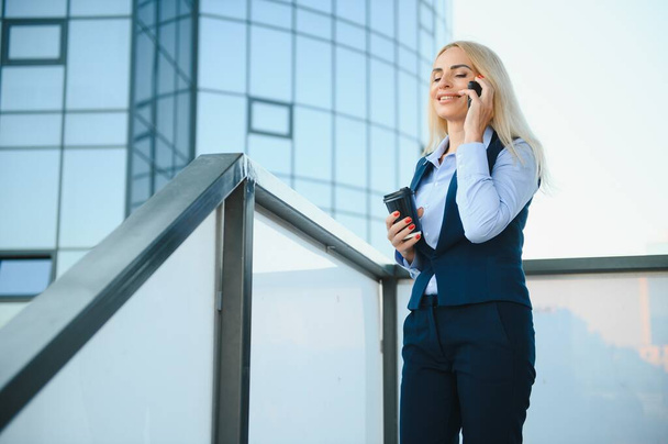 Business Woman With Phone Near Office. Portrait Of Beautiful Smiling Female In Fashion Office Clothes Talking On Phone While Standing Outdoors. Phone Communication. High Quality Image - Фото, зображення