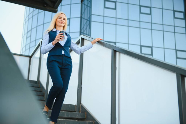 Beautiful Woman Going To Work With Coffee Walking Near Office Building. Portrait Of Successful Business Woman Holding Cup Of Hot Drink - Photo, Image